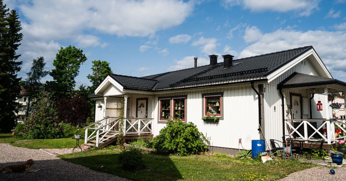Vit fin villa, en sommardag. Blå himmel med lätta slöjmoln och en hund som vilar på grusgången framför huset.